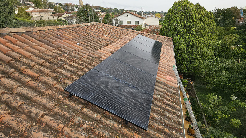 Panneaux solaires noirs installés sur un toit en tuiles rouges avec vue sur un quartier résidentiel et verdoyant.