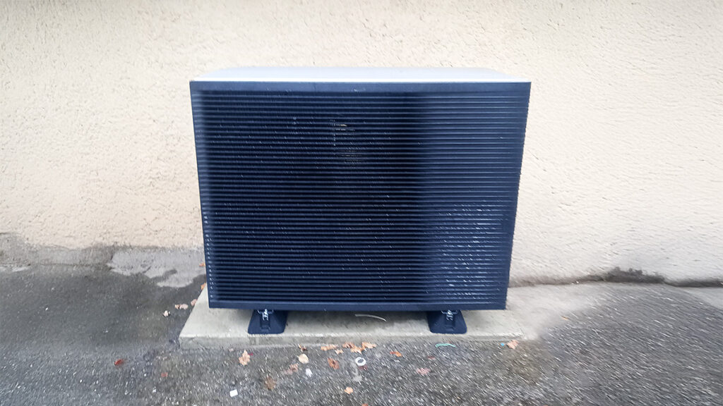 Unité extérieure de climatisation noire près d'un mur texturé clair sur le béton humide.