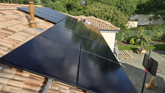 Panneaux solaires installés sur un toit, à proximité d'une cheminée et d'un jardin.