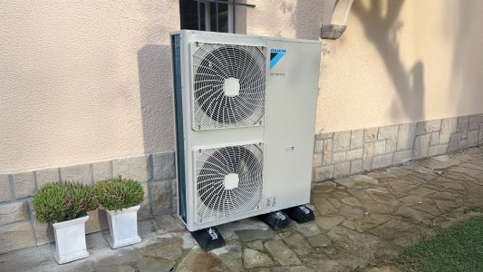 Climatiseur Daikin Altherma installé contre le mur d'une maison avec des plantes en pots.
