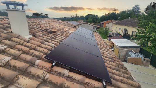 Panneaux solaires installés sur un toit en tuiles rouges avec vue sur des maisons et le ciel crépusculaire.