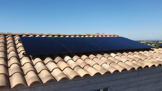 Panneaux solaires sur un toit en tuiles, avec ciel bleu en arrière-plan et paysage urbain en arrière-plan.