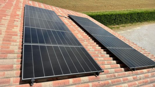 Panneaux solaires noirs sur un toit de tuiles rouges, dans un environnement rural.