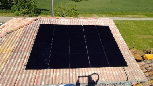 Panneaux solaires noirs installés sur le toit d'une maison en tuiles, vue aérienne.