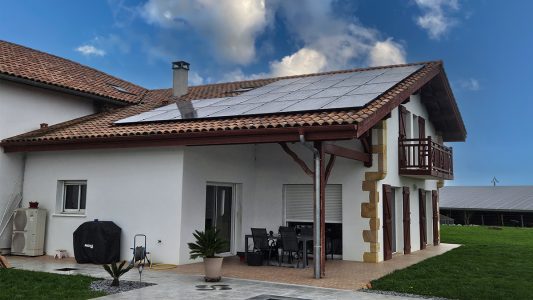 Maison avec panneaux solaires sur le toit et ciel bleu nuageux, énergie verte et durable.