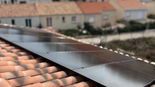 Panneaux solaires sur un toit en tuiles rouges, avec des maisons en arrière-plan.