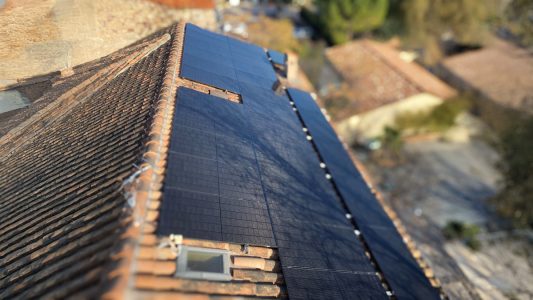 Panneaux solaires sur un toit en tuiles, vue plongeante sur un bâtiment ancien avec un paysage en arrière-plan.