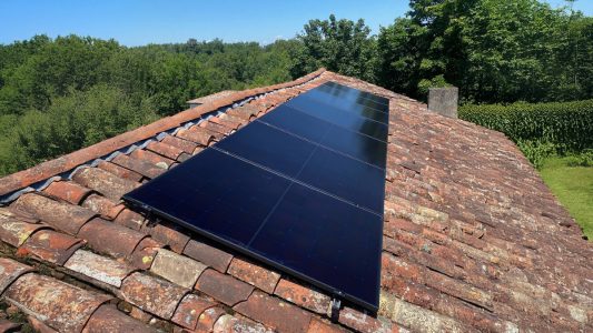 Panneaux solaires sur un toit en tuiles avec un arrière-plan de verdure et un ciel bleu clair.